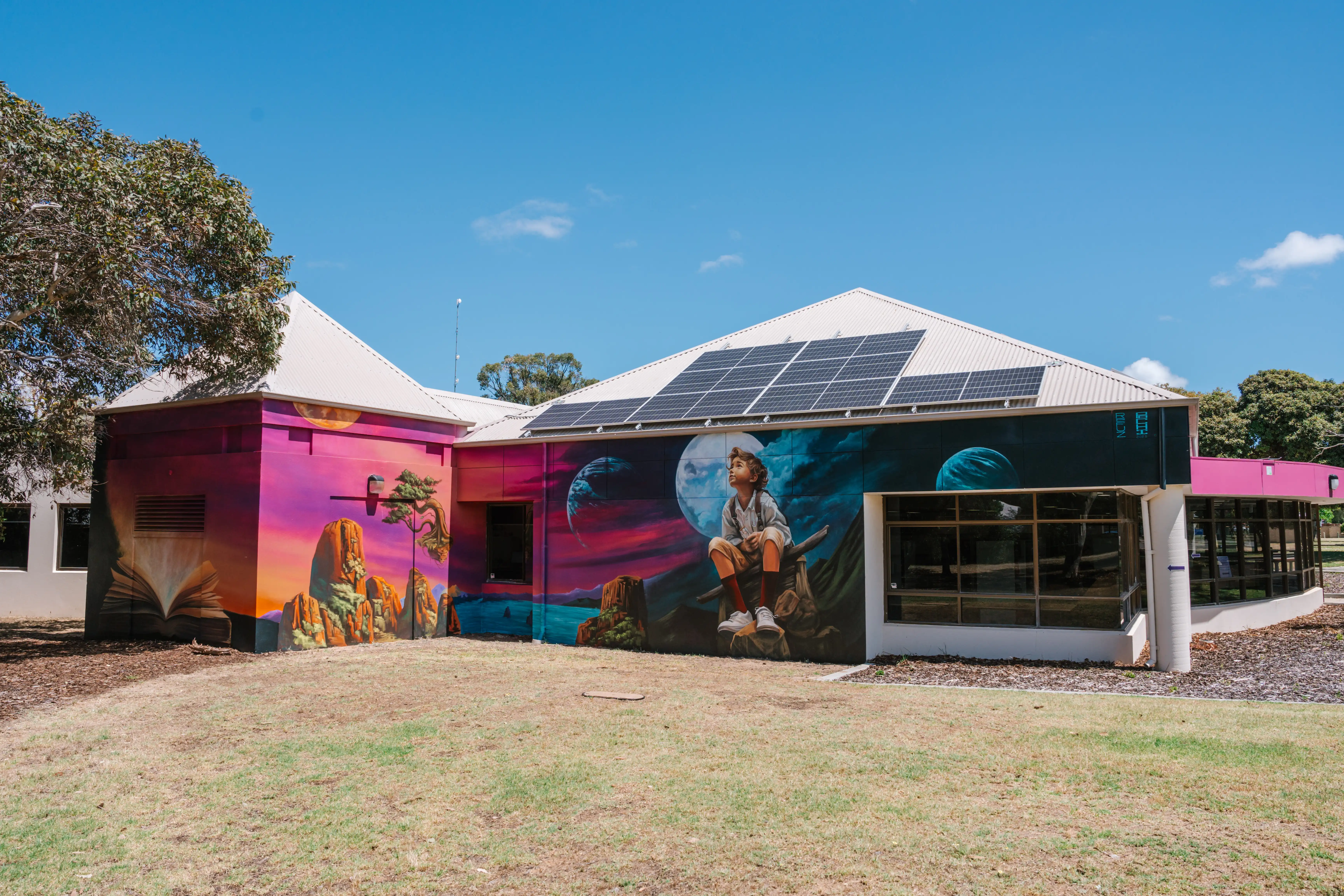A colourful mural on a building showing a person sitting with a cosmic backdrop and landscapes.